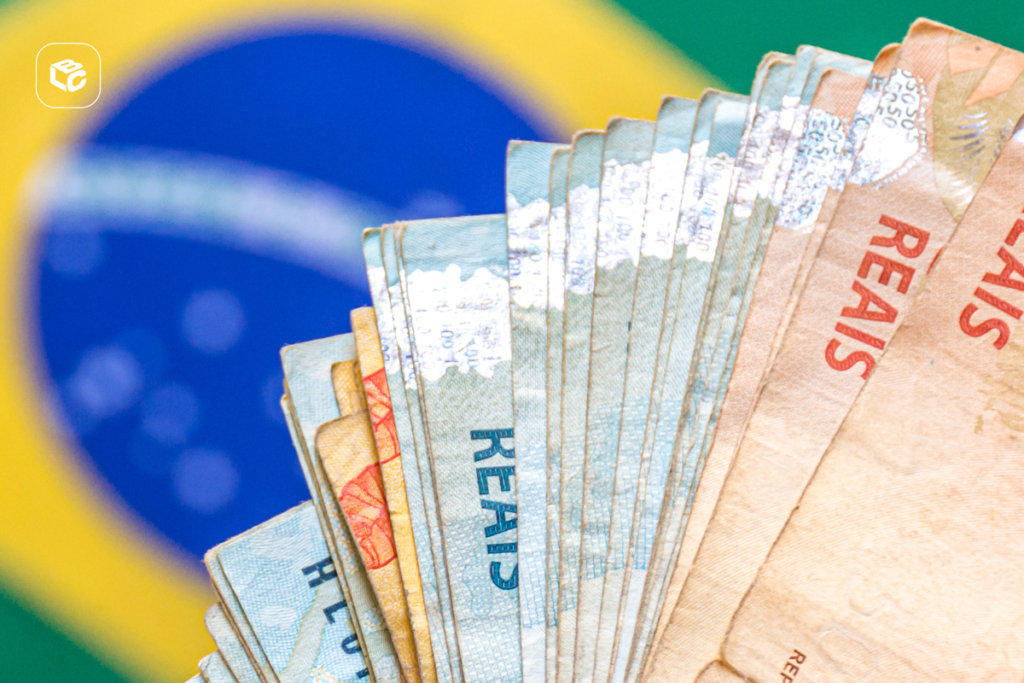 Notas de Real brasileiras em leque sobre a bandeira do Brasil.
