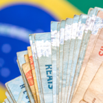 Notas de Real brasileiras em leque sobre a bandeira do Brasil.