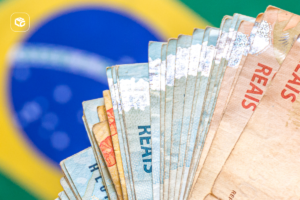 Notas de Real brasileiras em leque sobre a bandeira do Brasil.